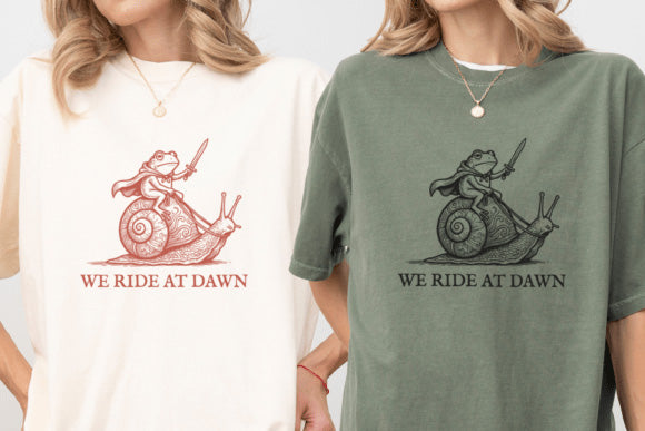 Black graphic tee from Anchored Grace Boutique with "We Ride at Dawn" design, casual fit, and bold white text on the front.