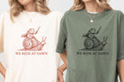 Black graphic tee from Anchored Grace Boutique with "We Ride at Dawn" design, casual fit, and bold white text on the front.