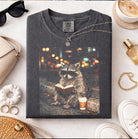 Reading Raccoon graphic tee from Anchored Grace Boutique featuring a cute raccoon reading a book on soft fabric.
