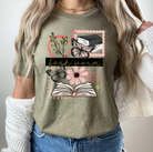 Graphic tee featuring Book Worm Stamps design from Anchored Grace Boutique, with colorful book and stamp illustrations.