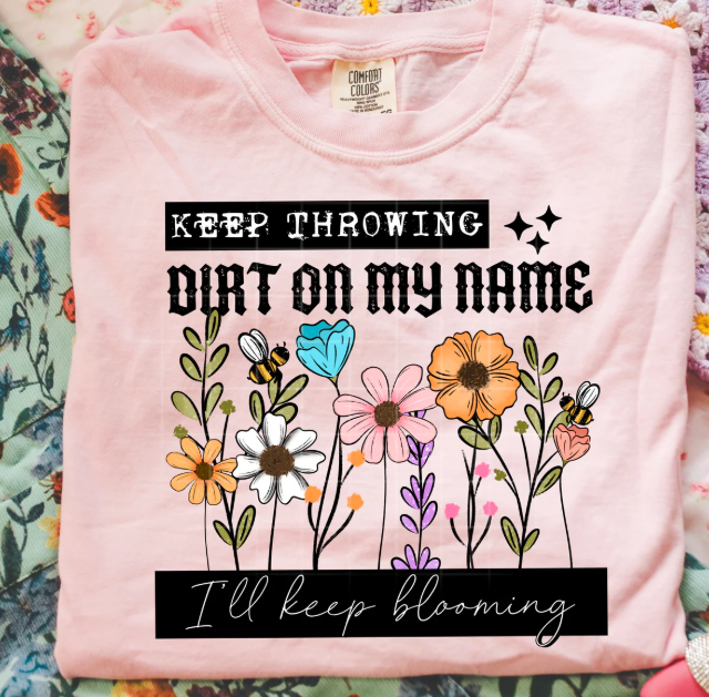 Blue graphic tee with "I'll Keep Blooming" design from Anchored Grace Boutique, featuring floral and uplifting artwork.