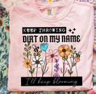 Blue graphic tee with "I'll Keep Blooming" design from Anchored Grace Boutique, featuring floral and uplifting artwork.
