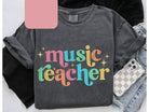 Music teacher graphic tee featuring musical notes and a playful design, stylishly worn, by Anchored Grace Boutique.