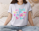 Pink graphic tee from Anchored Grace Boutique with "In a World Where You Can Be Anything Be Kind" slogan, casual and positive style.