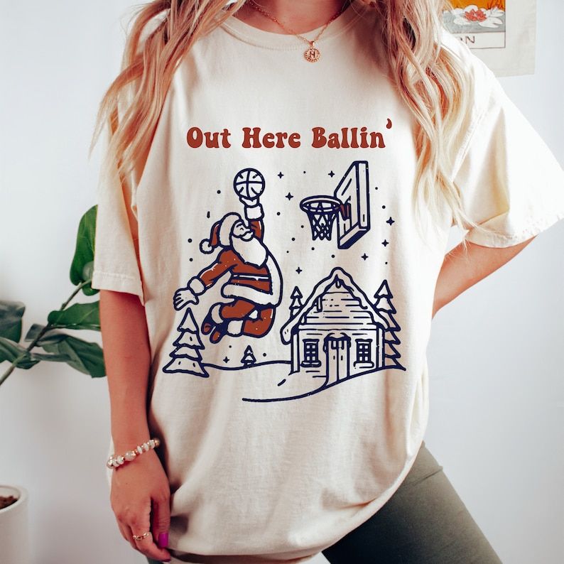 Out Here Ballin graphic tee by Anchored Grace Boutique, featuring bold text and casual style, worn by a model.