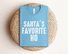 Red graphic tee featuring "Santa's Favorite Ho" slogan from Anchored Grace Boutique, with festive holiday design.