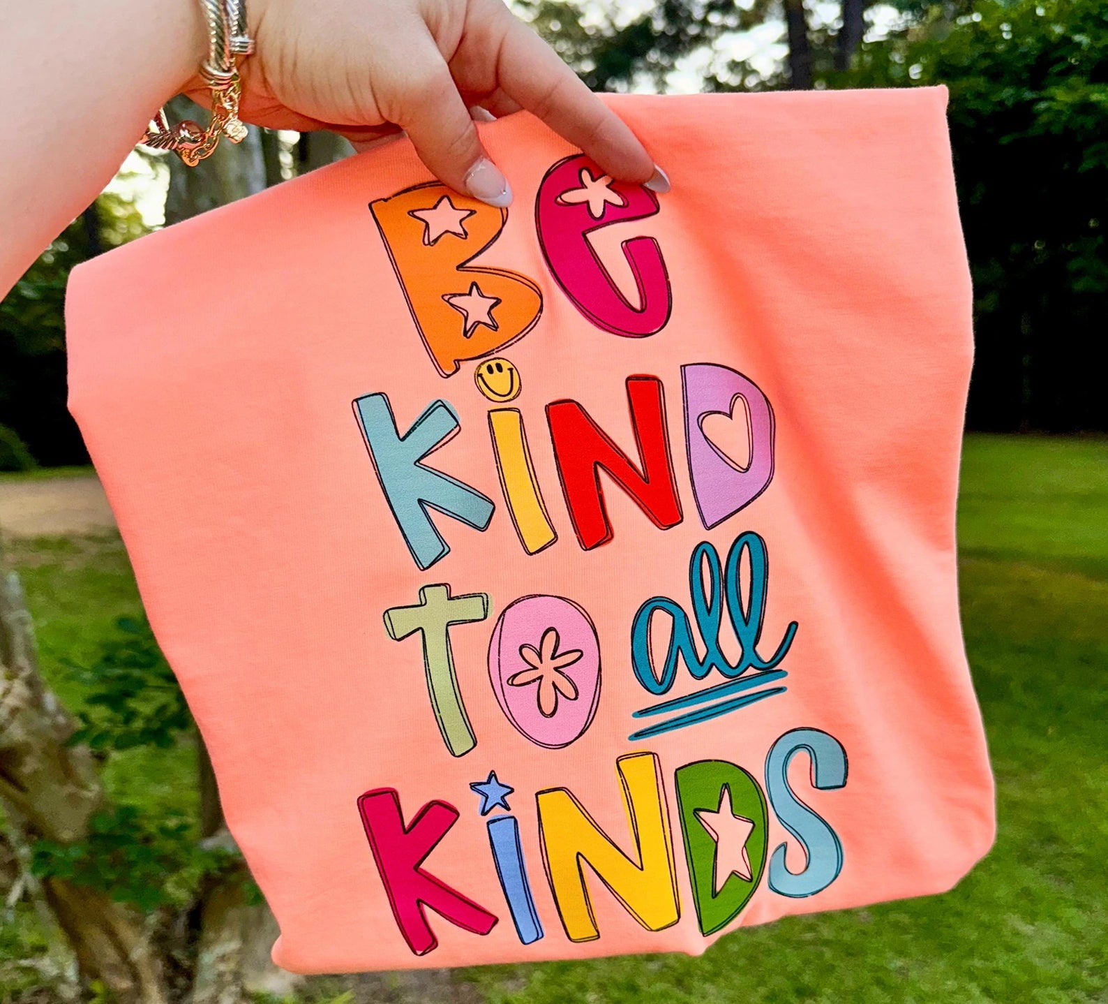 Be Kind to All Kinds graphic tee from Anchored Grace Boutique, featuring colorful text and diverse illustrations on soft fabric.