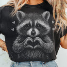 Black and white raccoon graphic tee from Anchored Grace Boutique, featuring a playful raccoon illustration on a casual t-shirt.