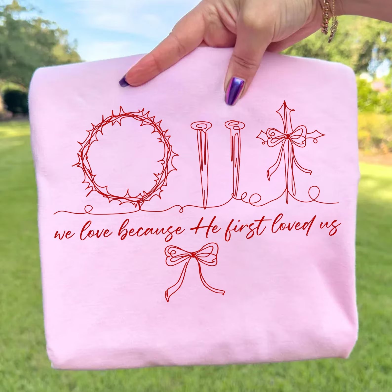Christian graphic tee featuring the message "We Love Because He First Loved Us" from Anchored Grace Boutique, with a stylish design.
