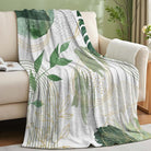 Sage green leaf throw blanket by CozyNest Decor with gold accents, soft flannel, mid-century boho style, 50x60 inches on a sofa.