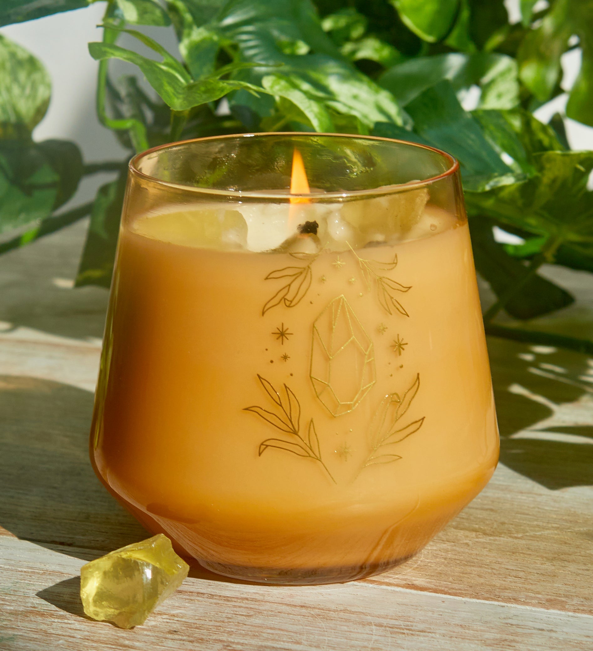 Citrine crystal healing scented glass candle on a wooden table, surrounded by decorative items in a cozy home interior.