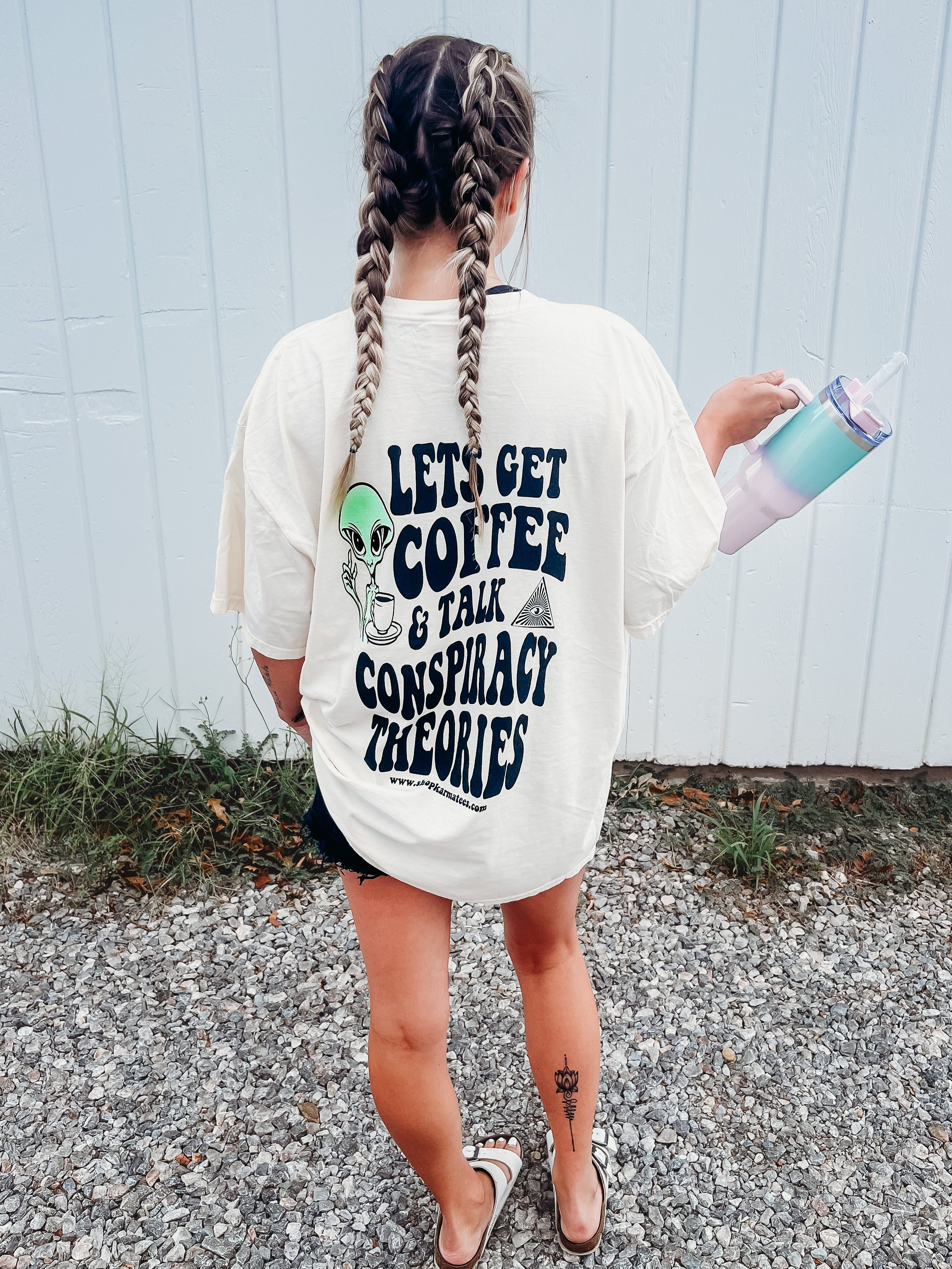 Black graphic tee featuring coffee cups and conspiracy theory illustrations, stylishly displayed on a hanger.