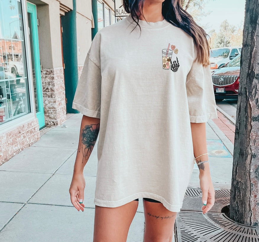 Black cotton t-shirt featuring "Fueled by Cafecito Y Chisme" graphic from Shop Karma Tees, displayed flat with folded sleeves.