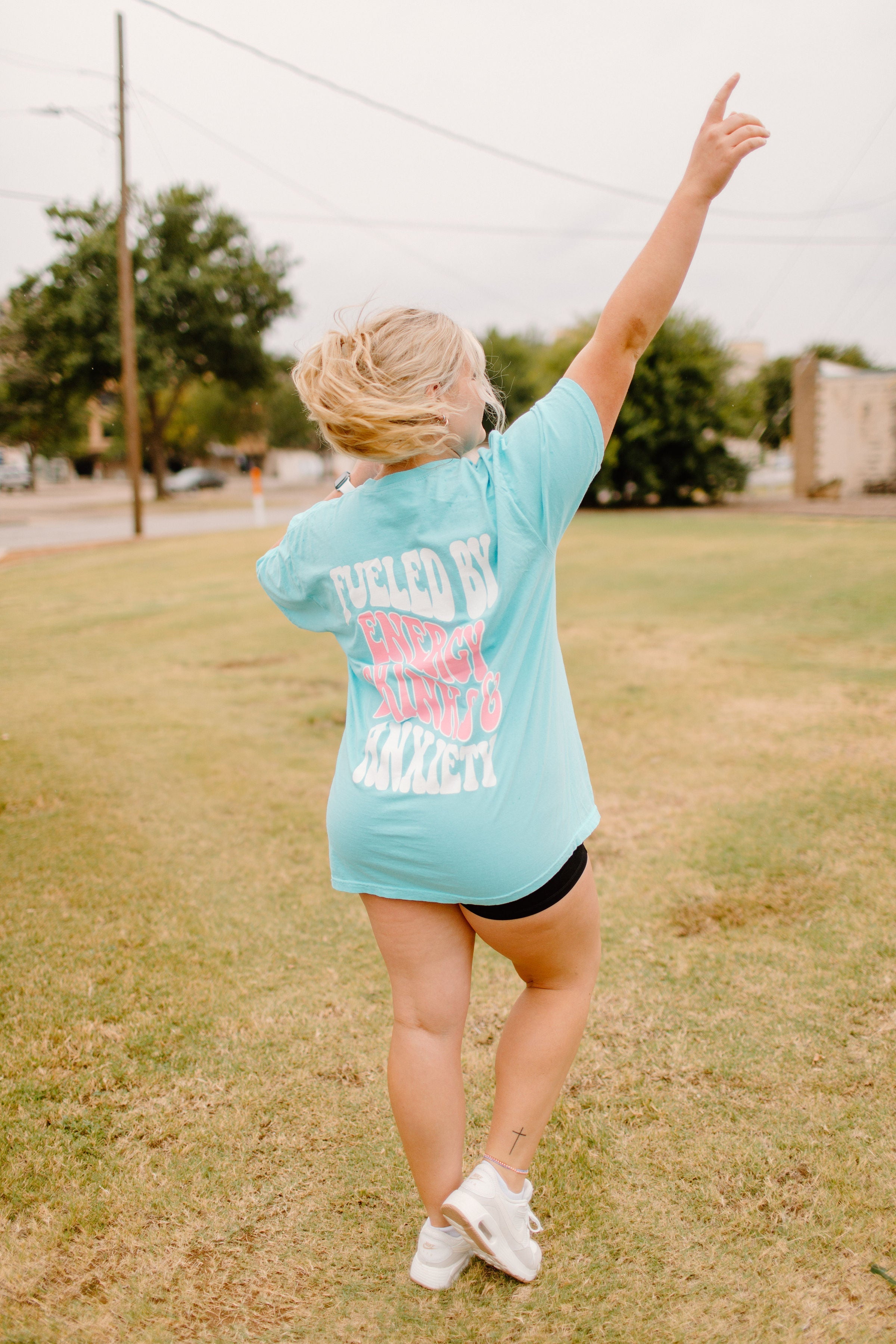 Graphic tee featuring "Fueled By Energy Drinks and Anxiety" design from Shop Karma Tees, with bold text and stylish streetwear style.