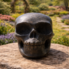 Shiny pyrite skull with detailed facial features and metallic gold finish, resting on a neutral background.
