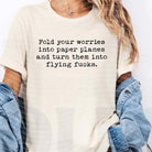 Fold Your Worries Into Paper Planes graphic tee by Anchored Grace Boutique, featuring a white t-shirt with a playful paper plane design.