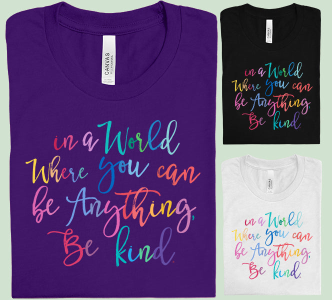 Light gray graphic tee from Anchored Grace Boutique with "In a World Where You Can Be Anything Be Kind" text in black lettering.
