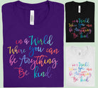 Light gray graphic tee from Anchored Grace Boutique with "In a World Where You Can Be Anything Be Kind" text in black lettering.