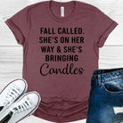 White graphic tee by Anchored Grace Boutique featuring fall-themed text "She's on Her Way and She's Bringing Candles" on the front.