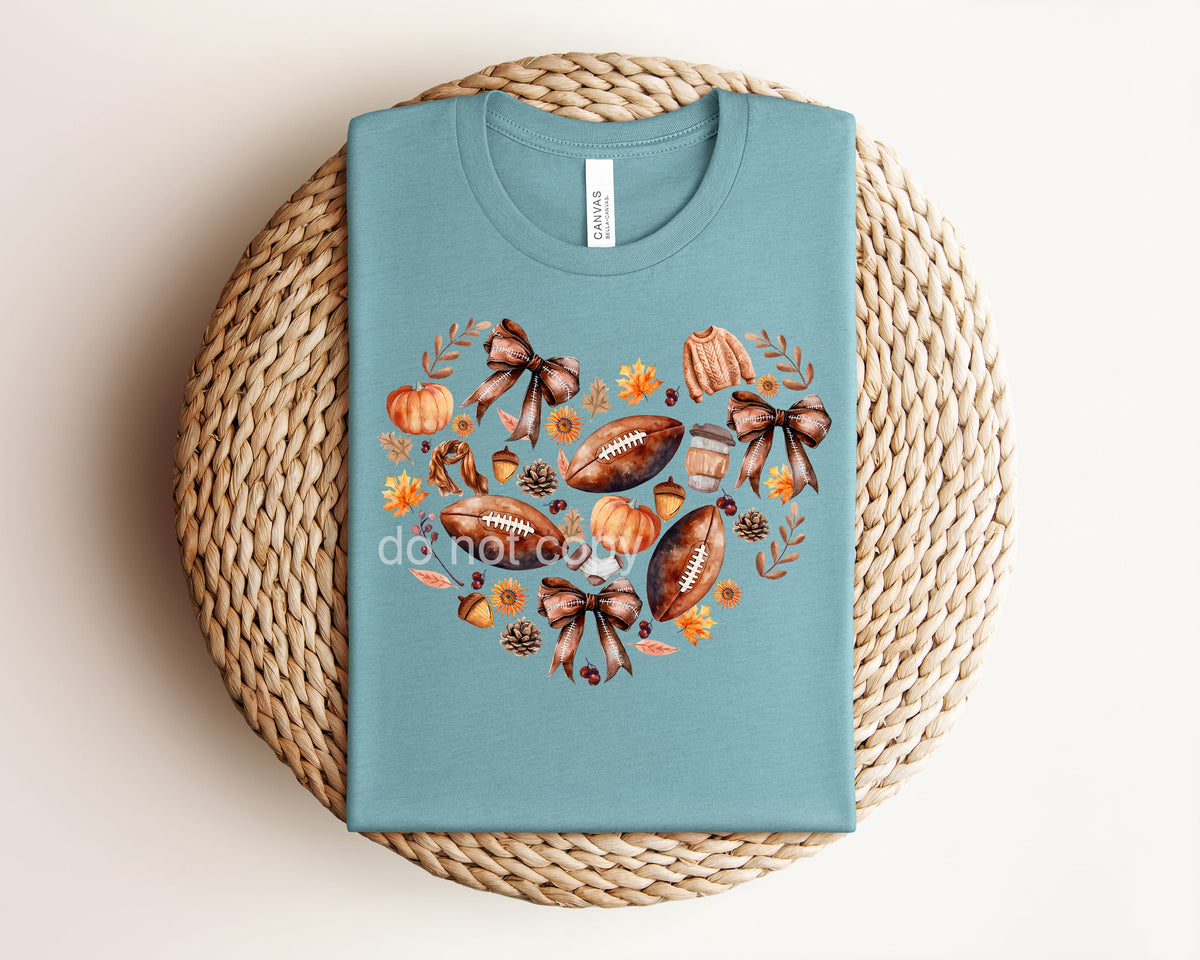 White fall football heart graphic tee by Anchored Grace Boutique featuring a seasonal football and heart design.