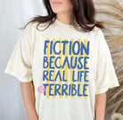 Black graphic tee from Anchored Grace Boutique with "Because Real Life is Terrible" text, casual fit, and soft cotton fabric.