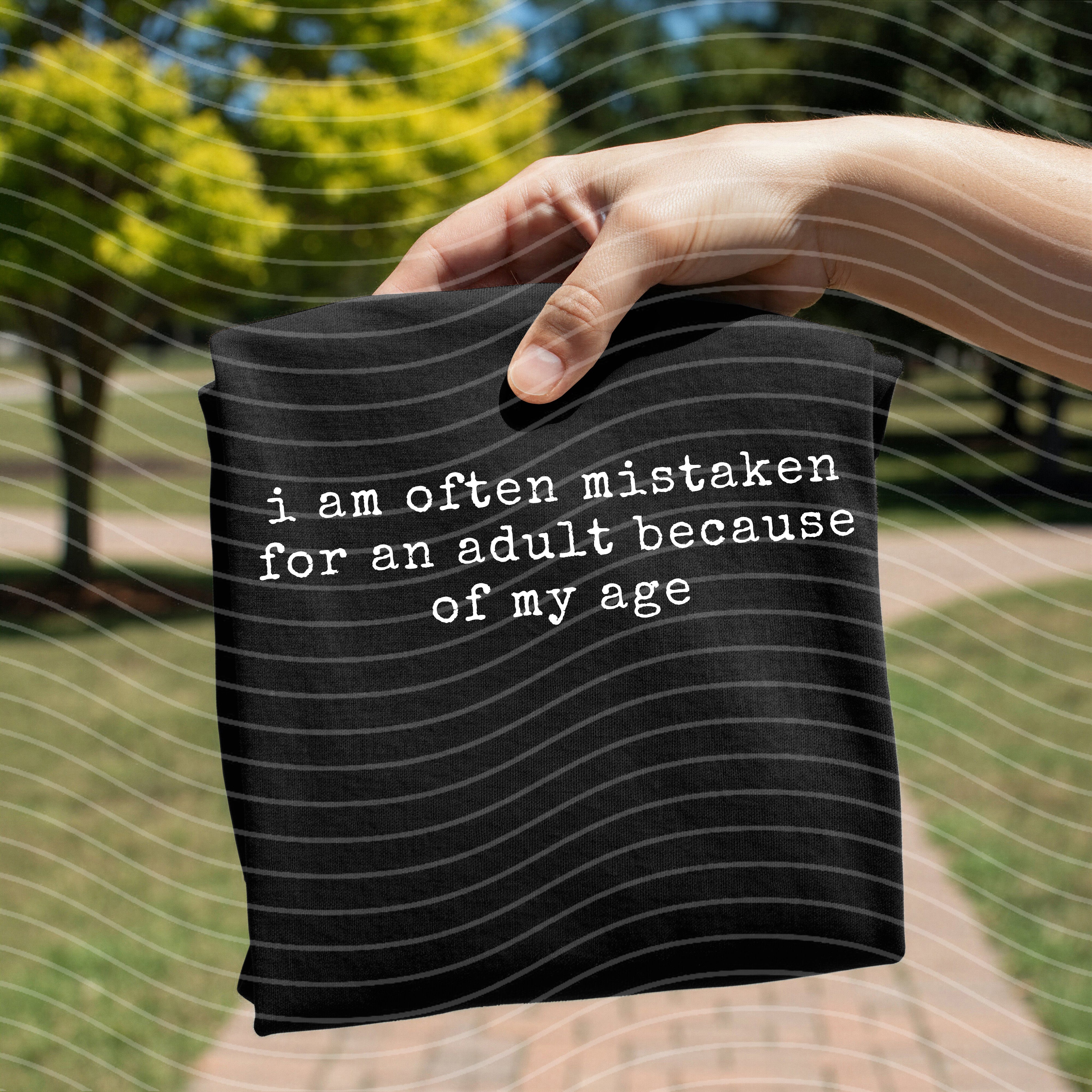 Gray graphic tee by Anchored Grace Boutique with "I am Often Mistaken for an Adult" print, casual fit, displayed on a hanger.