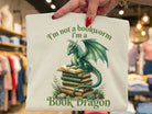 Colorful "I'm a Book Dragon" graphic tee by Anchored Grace Boutique featuring a whimsical dragon and book illustration.