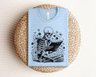 Black Reading Skelly graphic tee by Anchored Grace Boutique featuring a skeleton reading a book on the front.