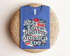 White graphic tee from Anchored Grace Boutique featuring "She Loves Jesus & America Too" message, casual style, and comfortable fit.