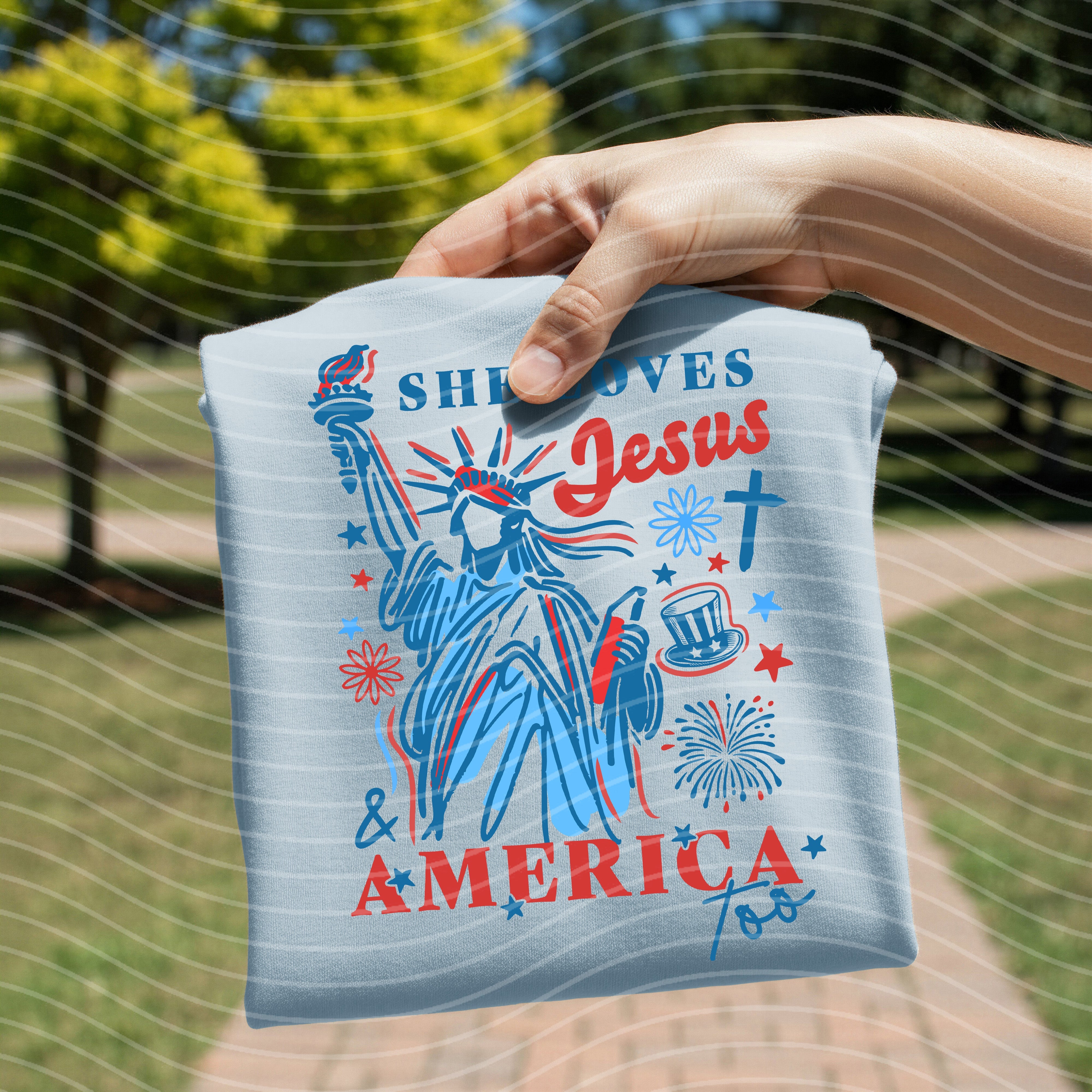 She Loves Jesus and America Too graphic tee by Anchored Grace Boutique, featuring patriotic and faith-inspired design.