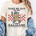 White graphic tee from Anchored Grace Boutique featuring "Take Me Out to the Ball Game" design, casual and stylish for sports fans.