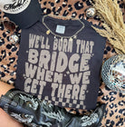 Black graphic tee from Anchored Grace Boutique featuring the phrase "We'll Burn That Bridge When We Get There" in bold white lettering.