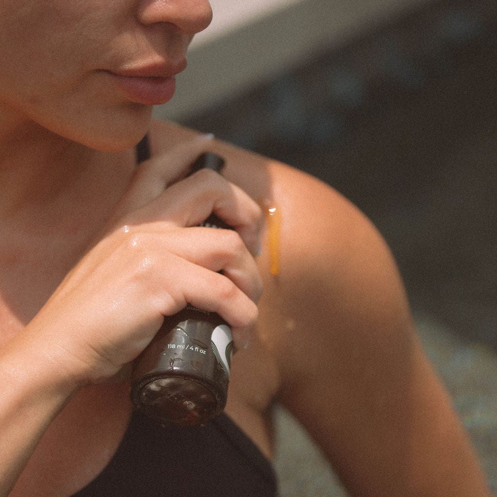 Woman applying Apoterra Vitamin C Body Oil in a bath and body setting, highlighting the nourishing skincare product.