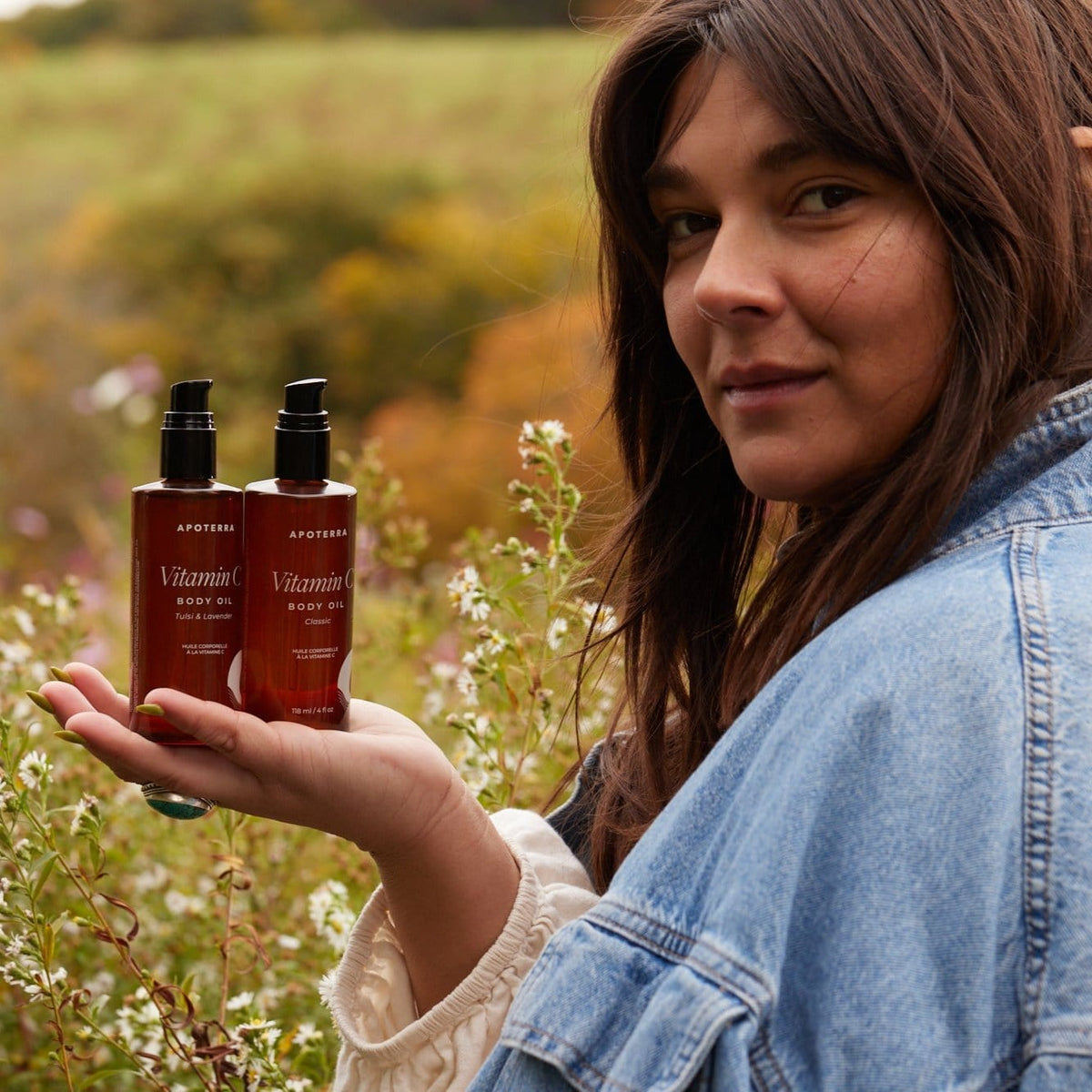 Apoterra Vitamin C Body Oil in a bath and body product bottle, model holding the bottle showing its packaging.