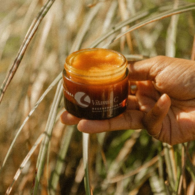 Woman holding a jar of Apoterra Vitamin C Regenerative Balm facial oil, showcasing the skincare product in a natural setting.