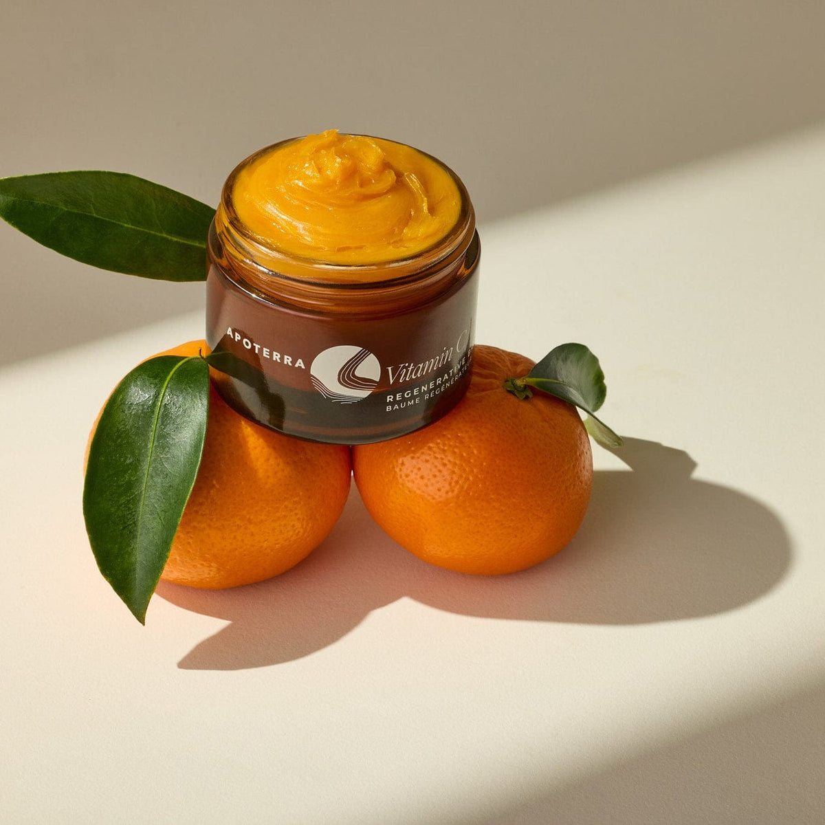Apoterra Vitamin C Regenerative Facial Oil balm with oranges, showcasing the nourishing skincare product in a natural setting.
