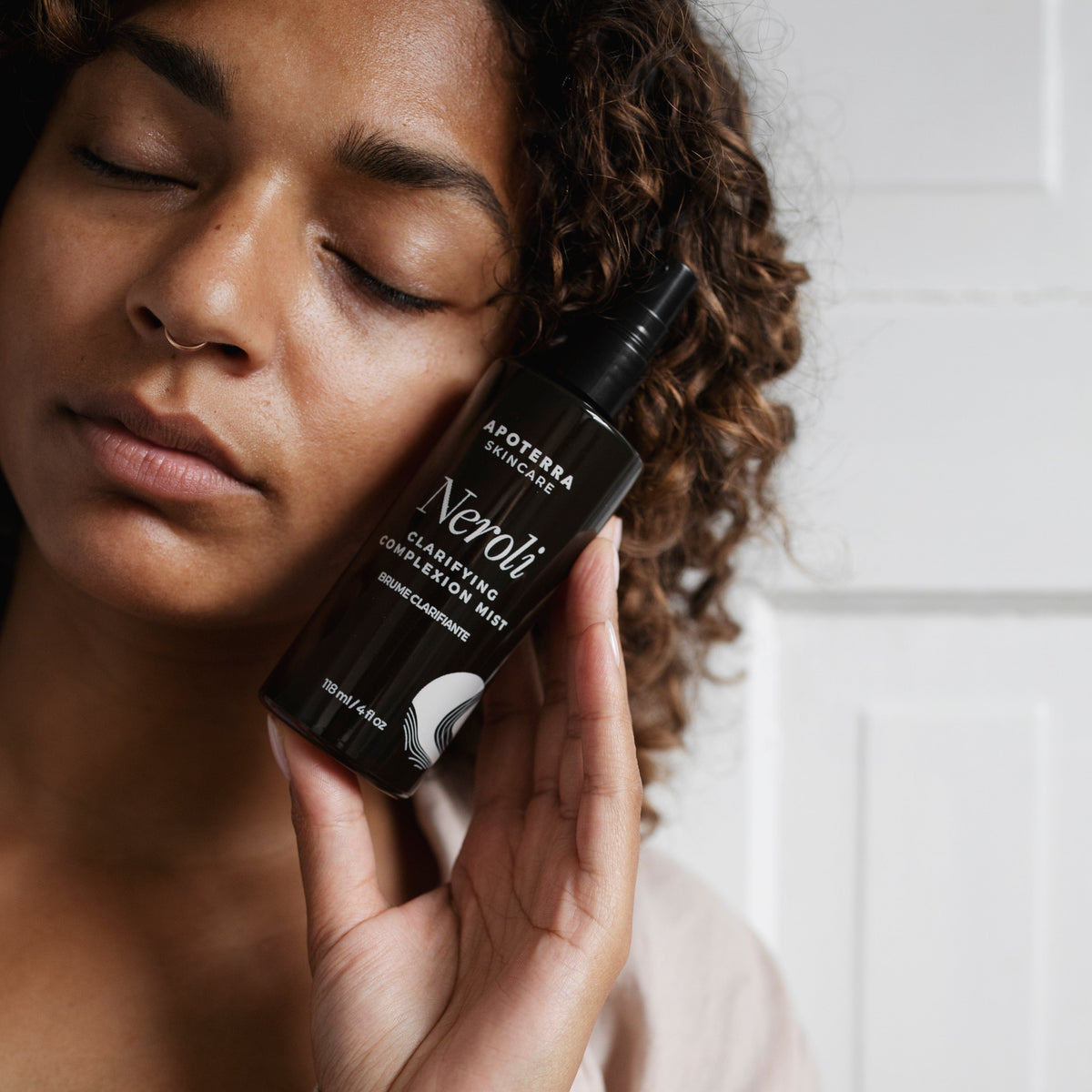 Apoterra Neroli Clarifying Complexion Mist toner bottle held by a model, showcasing the natural skincare product for glowing skin.
