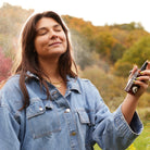 Woman spraying Apoterra Neroli Clarifying Complexion Mist outdoors, refreshing toner for clear, radiant skin.