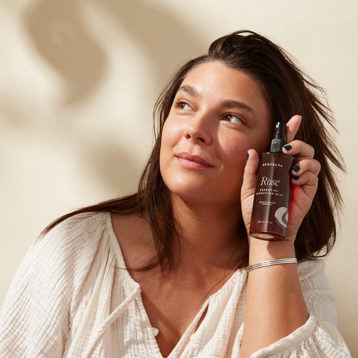 Apoterra Rose Essential Hydration Mist toner spray with rose water in a clear bottle, misting a woman's face for hydration.