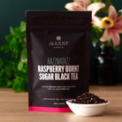Razzmatazz Raspberry Burnt Sugar Black Tea bag from August Uncommon Tea, featuring a colorful label and tea bag inside.