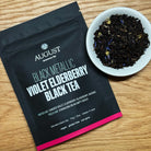 Black metallic tin of August Uncommon Tea Violet Elderberry Black Tea, a black tea beverage in a decorative metal container.