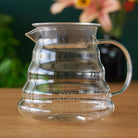 Two cup glass teapot by August Uncommon Tea showing clear glass design with a metal handle and lid, perfect for brewing tea.