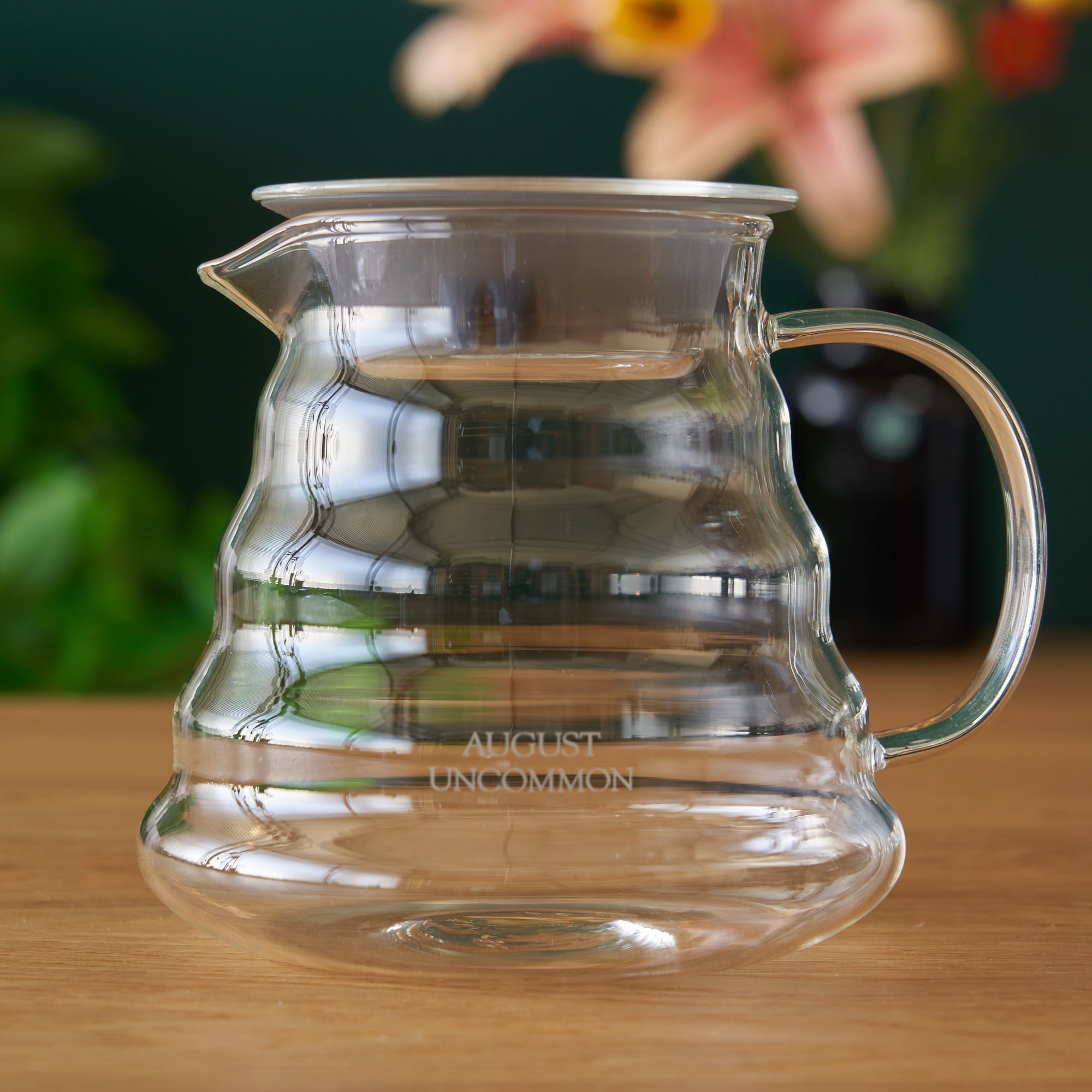 Two cup glass teapot by August Uncommon Tea showing clear glass design with a metal handle and lid, perfect for brewing tea.