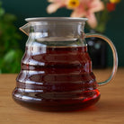 Two cup glass teapot by August Uncommon Tea, showcasing clear glass body, lid, and handle, ideal for brewing and serving tea.
