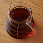 Two cup glass teapot by August Uncommon Tea, showcasing clear glass body and stainless steel lid for brewing tea.
