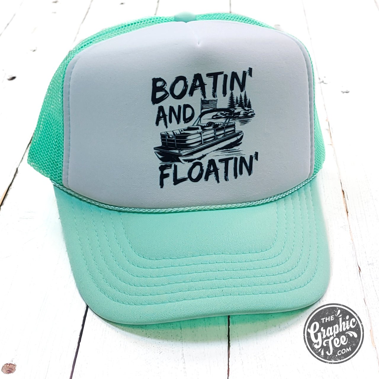 Seafoam and white foam trucker cap by The Graphic Tee, featuring embroidered boating and floating design, adjustable mesh back.