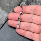 Pink Rose Quartz Skull Obelisk dangle belly ring from BodyCandy featuring a rose quartz skull design and dangling rose accents.