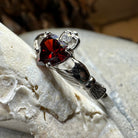 Celtic Crystal Design Jewelry Garnet Claddagh Ring showing a detailed gold band with a heart and crown motif featuring a deep red garnet gemstone.