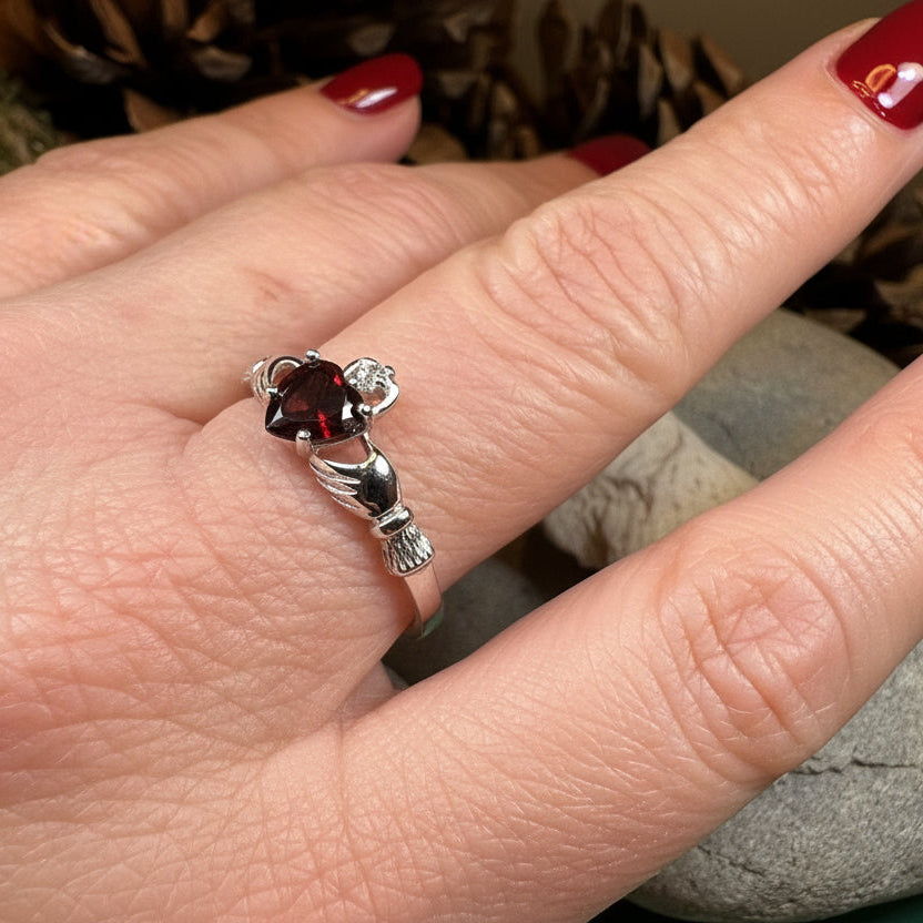 Garnet Claddagh ring by Celtic Crystal Design Jewelry featuring a detailed gold-tone band and a central red garnet gemstone.