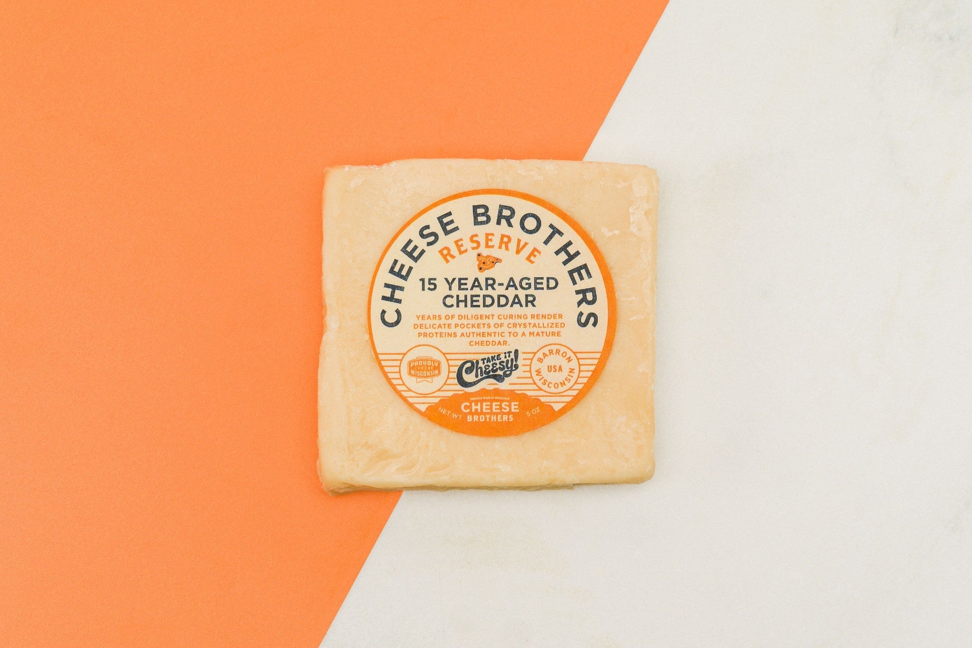 A block of 15-year-aged cheddar cheese from Cheese Brothers, Inc., showcasing its rich, firm texture and deep golden color.
